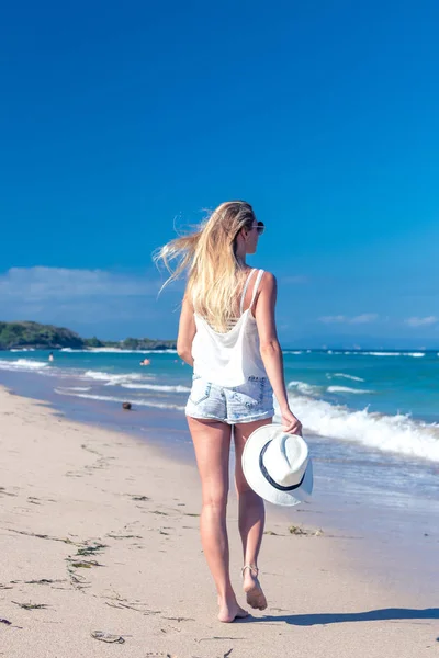 Jonge sexy vrouw met witte hoed wandelen op witte zand strand een tropisch eiland Bali's zonnige dag. Kosten van de Oceaan. — Stockfoto