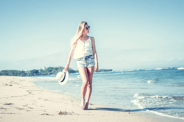 Mujer sexy joven con sombrero blanco caminando en la playa de arena blanca una isla tropical de Bali en el día soleado. Coste del océano . — Foto de Stock