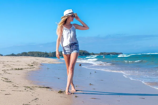 Mujer sexy joven con sombrero blanco caminando en la playa de arena blanca una isla tropical de Bali en el día soleado. Coste del océano . — Foto de Stock