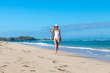 Beyaz şapka üzerinde beyaz kum plaj tropikal bir Bali Adası güneşli gün yürüyüş ile genç seksi kadın. Okyanus maliyet.