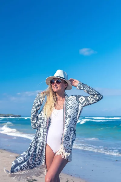 Beyaz şapka ve güneş gözlüğü üzerinde beyaz kum plaj tropikal bir Bali Adası güneşli gün yürüyüş olan seksi bir kadın portresi. Okyanus maliyet. — Stok fotoğraf