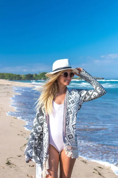 Retrato de una joven mujer sexy con sombrero blanco y gafas de sol caminando en la playa de arena blanca una isla tropical de Bali en un día soleado. Coste del océano . — Foto de Stock