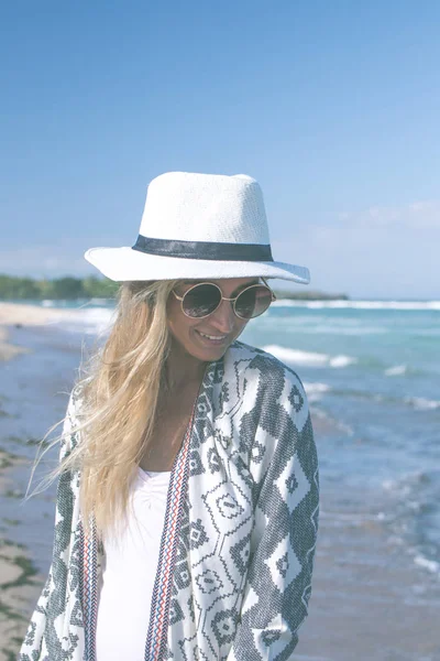 Retrato de una joven mujer sexy con sombrero blanco y gafas de sol caminando en la playa de arena blanca una isla tropical de Bali en un día soleado. Coste del océano . — Foto de Stock