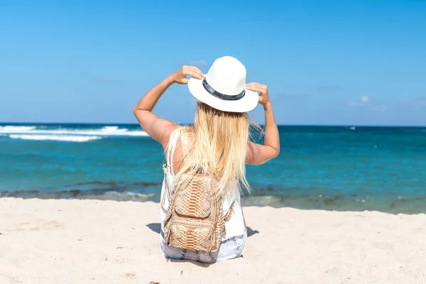 Jonge sexy vrouw met witte hoed en luxe slangenhuid python rugzak zit op witte zand strand een tropisch Bali eiland op zonnige dag. Kosten van de Oceaan. — Stockfoto
