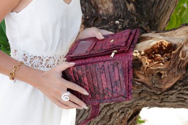 Yakın çekim genç kadın elle lüks pahalı yılan derisi python cüzdan. Asya bitki ve ağaç arka plan üzerinde. Bali, Endonezya.