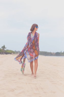 Güneş gözlüğü ve plaj çantası seyahat tatil günlerinde rahatlatıcı bir tropikal yaz tatil plaj üzerinde yürüyen kadın turist. Genç Bayan lüks moda beachwear, Bali Adası, Endonezya.