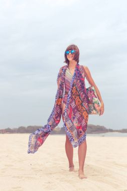 Güneş gözlüğü ve plaj çantası seyahat tatil günlerinde rahatlatıcı bir tropikal yaz tatil plaj üzerinde yürüyen kadın turist. Genç Bayan lüks moda beachwear, Bali Adası, Endonezya.