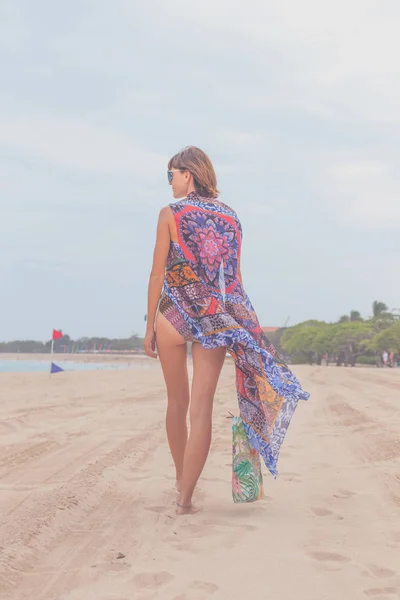 Γυναίκα τουριστικές περπατώντας σε μια τροπική καλοκαίρι διακοπές παραλία φορώντας γυαλιά ηλίου και τσάντα παραλίας ήσυχες και ξεκούραστες διακοπές. Νεαρή κοπέλα σε πολυτελή μαγιό μόδα, Μπαλί, Ινδονησία. — Φωτογραφία Αρχείου