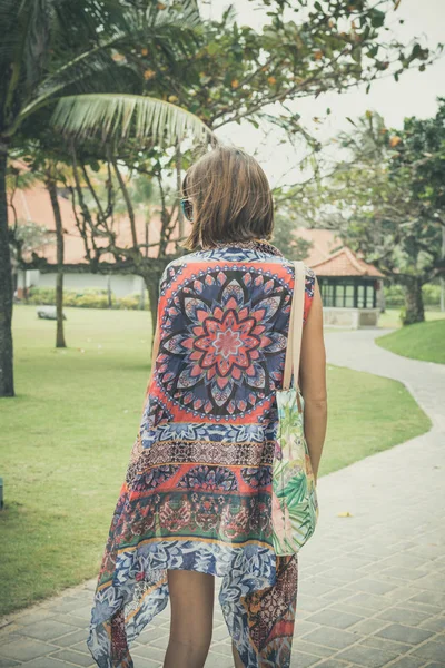 Hermosa mujer joven en pareo y traje de baño caminando en el parque becah con bolsa en el día soleado de verano. Isla tropical Bali, Indonesia . — Foto de Stock