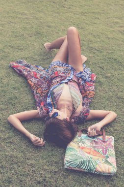 Otların arasında rahatlatıcı. Güzel genç kadın güneş gözlüğü ve plaj çantası tropikal Bali Adası, Endonezya'nın parkta ile yeşil çim üzerinde yalan pareo Üstten Görünüm.