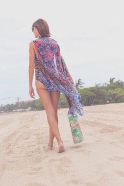 Güneş gözlüğü ve plaj çantası seyahat tatil günlerinde rahatlatıcı bir tropikal yaz tatil plaj üzerinde yürüyen kadın turist. Genç Bayan lüks moda beachwear, Bali Adası, Endonezya.