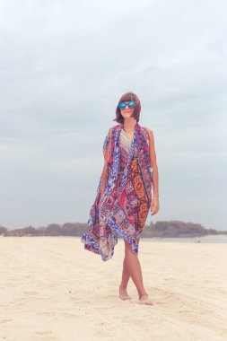Güneş gözlüğü ve plaj çantası seyahat tatil günlerinde rahatlatıcı bir tropikal yaz tatil plaj üzerinde yürüyen kadın turist. Genç Bayan lüks moda beachwear, Bali Adası, Endonezya.