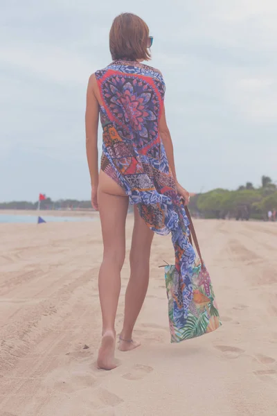 Touristin, die mit Sonnenbrille und Strandtasche an einem tropischen Sommerurlaubsstrand spazieren geht und sich im Urlaub entspannt. junge Dame in luxuriöser Mode Beachwear, Bali Island, Indonesien. — Stockfoto