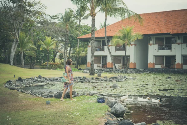 Eine Frau im Pareo füttert Graugänse und Gänse auf dem See in der Nähe eines Luxushotels in Nusa Dua, tropische Insel Bali, Indonesien. — Stockfoto