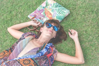 Otların arasında rahatlatıcı. Güzel genç kadın güneş gözlüğü ve plaj çantası tropikal Bali Adası, Endonezya'nın parkta ile yeşil çim üzerinde yalan pareo Üstten Görünüm.