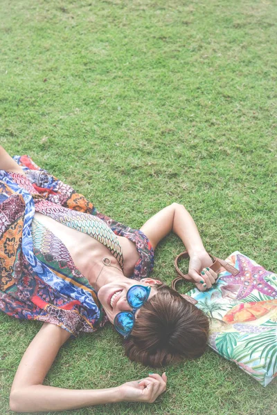 Otların arasında rahatlatıcı. Güzel genç kadın güneş gözlüğü ve plaj çantası tropikal Bali Adası, Endonezya'nın parkta ile yeşil çim üzerinde yalan pareo Üstten Görünüm.