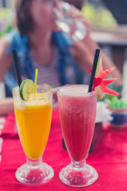 Taze karpuz ve portakal suları gözlük restoran ve kafe kırmızı tabloda buzlu iç. Bali, Endonezya'nın tropik ada. Bir arka plan üzerinde genç kadın.