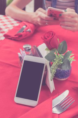 Boş beyaz ekran restoranda kırmızı zemin üzerine beyaz cep telefonuyla mockup görüntüsü. Tropikal Bali Adası, Endonezya. Arka plan bulanık smartphone ile kadın el.