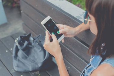 Parkta bir bankta oturmuş smartphone kullanan güzel genç seksi kadın. Bali Adası, Endonezya.