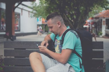 Mutlu genç yakışıklı üzerinde tezgah açık havada oturma ve smartphone kullanarak adam. Bali, Endonezya'nın tropik ada.