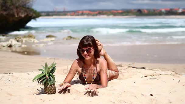 Sexy kobieta w brązowy strój kąpielowy na plaży z ananasem. Młoda kobieta korzystających lato wakacje na tropikalnej wyspie Bali, Indonezja. — Wideo stockowe