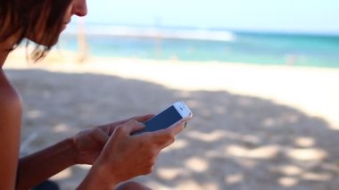 Kumsalda gülüyor mobil akıllı telefon kullanan kadın. Kız mutlu smartphone kullanarak bikini. Tropikal Bali Adası, Endonezya.