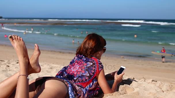 Kumsalda gülüyor mobil akıllı telefon kullanan kadın. Kız mutlu smartphone kullanarak bikini. Tropikal Bali Adası, Endonezya. — Stok video