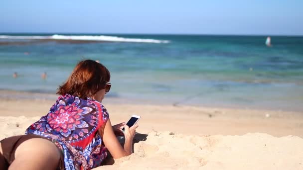 Kobieta za pomocą inteligentny telefon telefon komórkowy, śmiejąc się na plaży. Dziewczyna w bikini za pomocą smartphone szczęśliwy. Tropikalna wyspa Bali, Indonezja. — Wideo stockowe