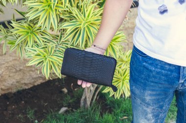 Adam tutarak el yapımı çanta egzotik deri yılan derisi python, açık havada, yeşil tropikal arka plan yaptı. Bali Adası.