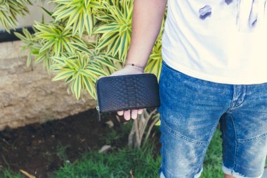 Adam tutarak el yapımı çanta egzotik deri yılan derisi python, açık havada, yeşil tropikal arka plan yaptı. Bali Adası.