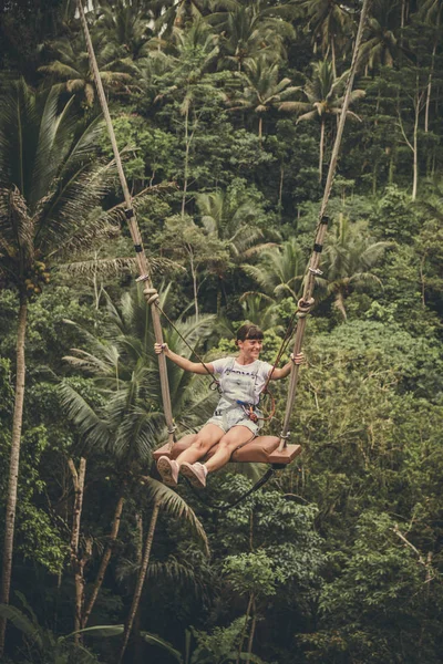Joven turista balanceándose sobre el acantilado en la selva tropical de una isla tropical de Bali, Indonesia . — Foto de Stock
