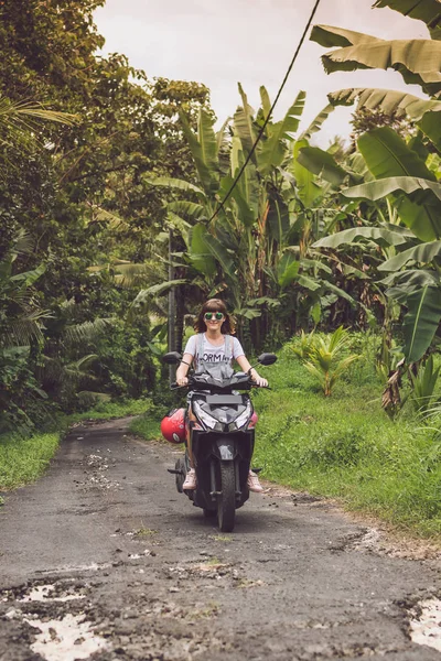 Jeune femme heureuse sur une moto dans la forêt tropicale tropicale de Bali, Indonésie. Concept de liberté. Dame sur un scooter . — Photo