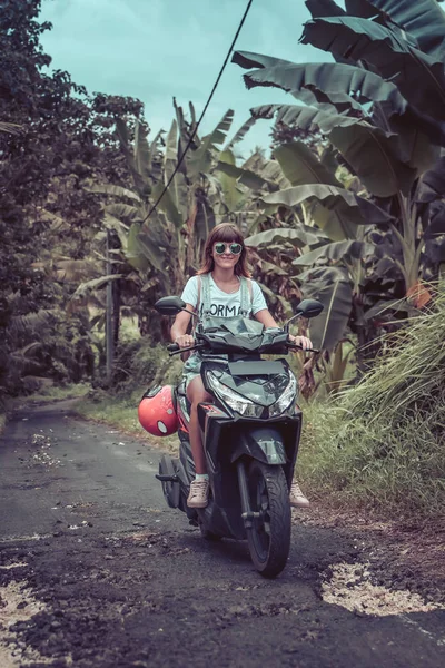 Joven mujer feliz en una moto en la selva tropical de una isla tropical de Bali, Indonesia. Concepto de libertad. Señora en un scooter . — Foto de Stock