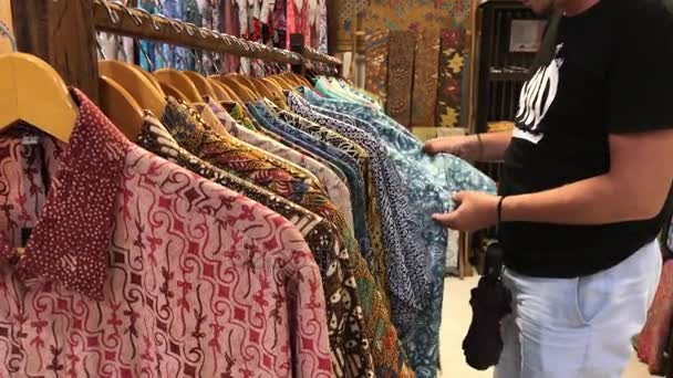 Man voor het kiezen van een balinese batik-shirt in de winkel. Winkelen voor mannen in Asia concept. Katoenen overhemd. — Stockvideo