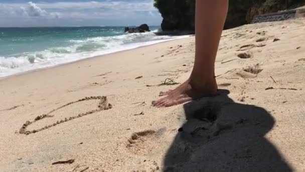 Genç çekici kadın bir kalp kumun üzerinde çizim. Tropikal plaj. Bali Adası, Endonezya. — Stok video