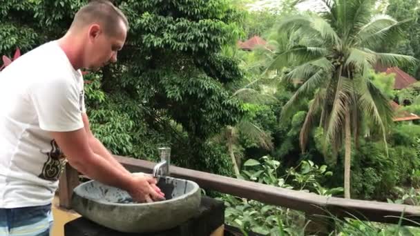 Homem lavando as mãos e rosto lá fora com uma bela vista tropical. Conceito de frescura e ecologia. Ilha de Bali . — Vídeo de Stock