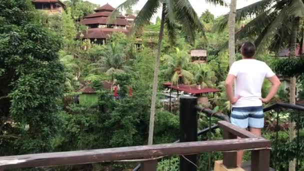 Bali, Indonésie - 14. února 2018: Mladý muž, stojící na terase a při pohledu na řeky. Tropické džungle na pozadí. Ostrov Bali. — Stock video