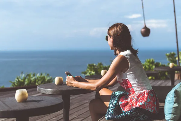 Woman sitting in a tropical restaurant with ocean view. Original place. Space for text. Bali island.