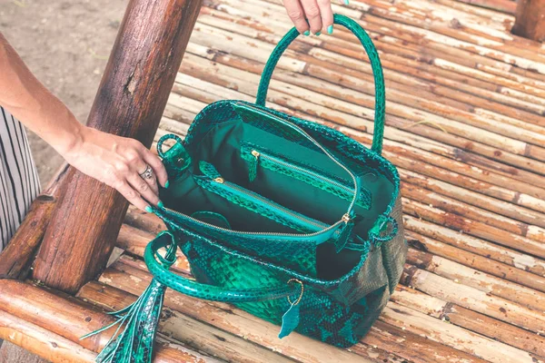 Woman hands with luxury snakeskin handbag outdoors. Tropical fashion exotic concept.