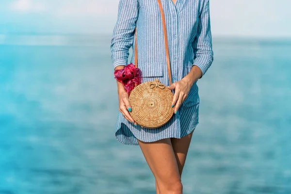 Женские руки с модной стильной сумкой из ротанга и шелковым шарфом на фоне океана. Тропический остров Бали, Индонезия. Сумочка из ротанга и шелковый шарф . — стоковое фото