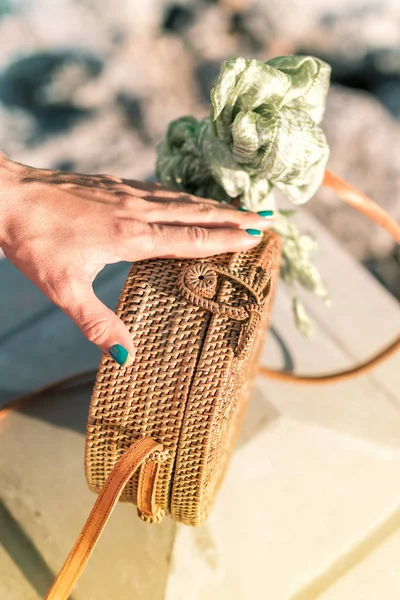 Mano de mujer con bolsa de ratán elegante de moda y bufanda de seda en el exterior. Isla tropical de Bali, Indonesia. Bolso de ratán y bufanda de seda . — Foto de Stock