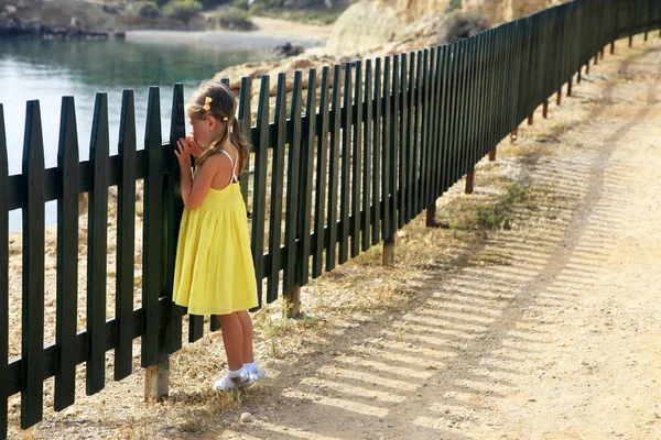 Κοριτσάκι κοιτάζει τη θάλασσα μέσα από ένα φράχτη — Φωτογραφία Αρχείου