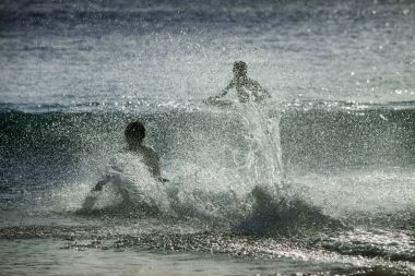 Okyanus su sıçramalarına batımında insan siluetleri