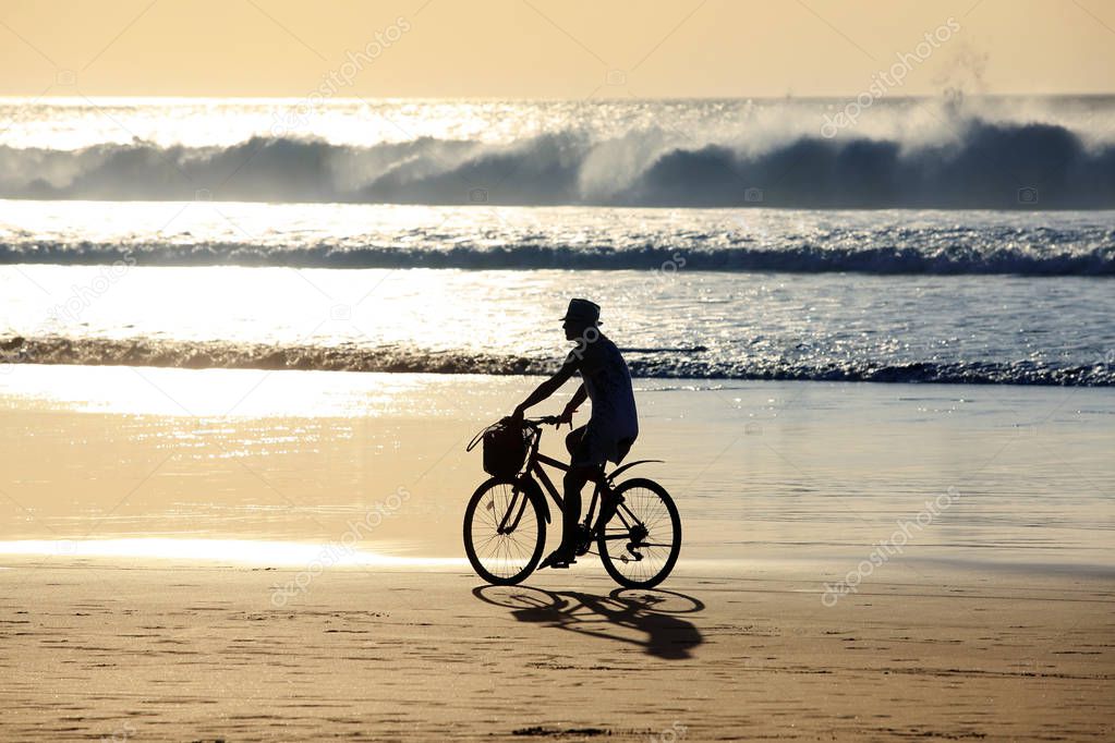 Girl on a bicycle is riding along the ocean at sunset