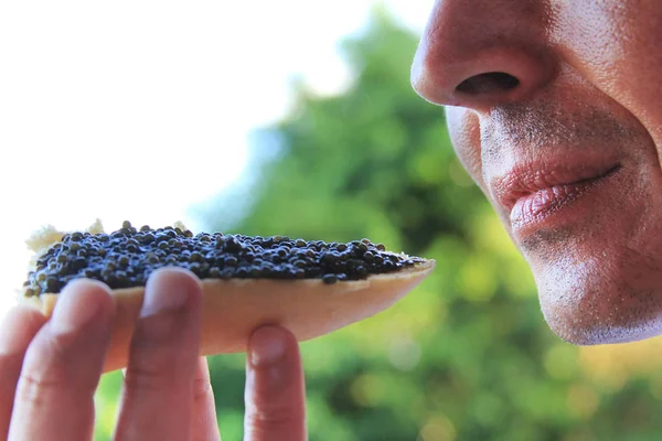 Homme adulte mangeant un sandwich au caviar noir — Photo