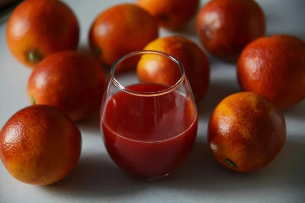 Κόκκινα πορτοκάλια Σικελίας γύρω από ένα ποτήρι με φρέσκο χυμό Royalty Free Φωτογραφίες Αρχείου