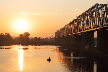 Gün doğumu. Geniş bir nehrin üzerindeki demiryolu köprüsü. Dinyeper Nehri, Kiev, Ukrayna. Teknedeki bir balıkçının silueti..