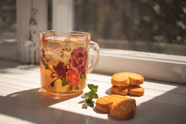 Травяной чай. Стакан с чаем стоит на подоконнике. Домашнее печенье в форме сердца — стоковое фото