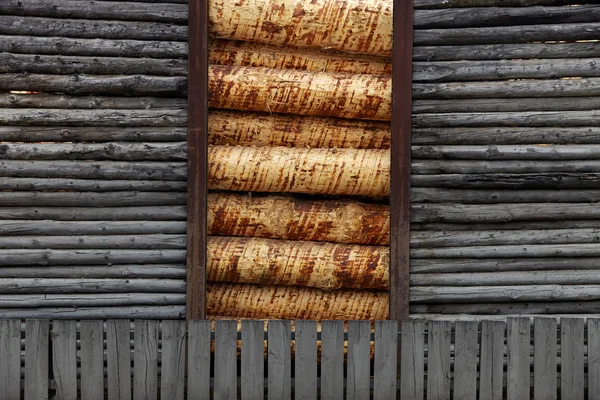 Old weathered log barn wall facade fragment and batten fence of rustic horizontal and vertical grey timber background loaded with freshly cut debarked pine wood lumber — Stock Photo, Image