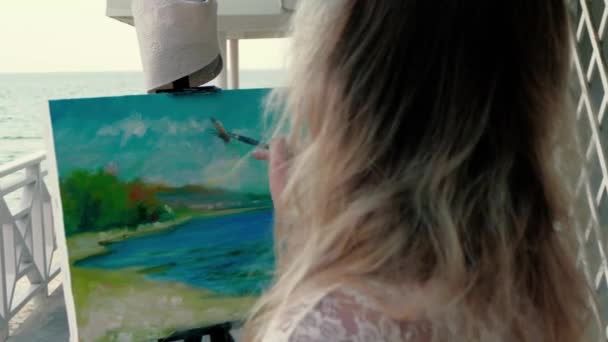Jovem artista pintando uma paisagem marítima em pé no terraço da praia de madeira — Vídeo de Stock
